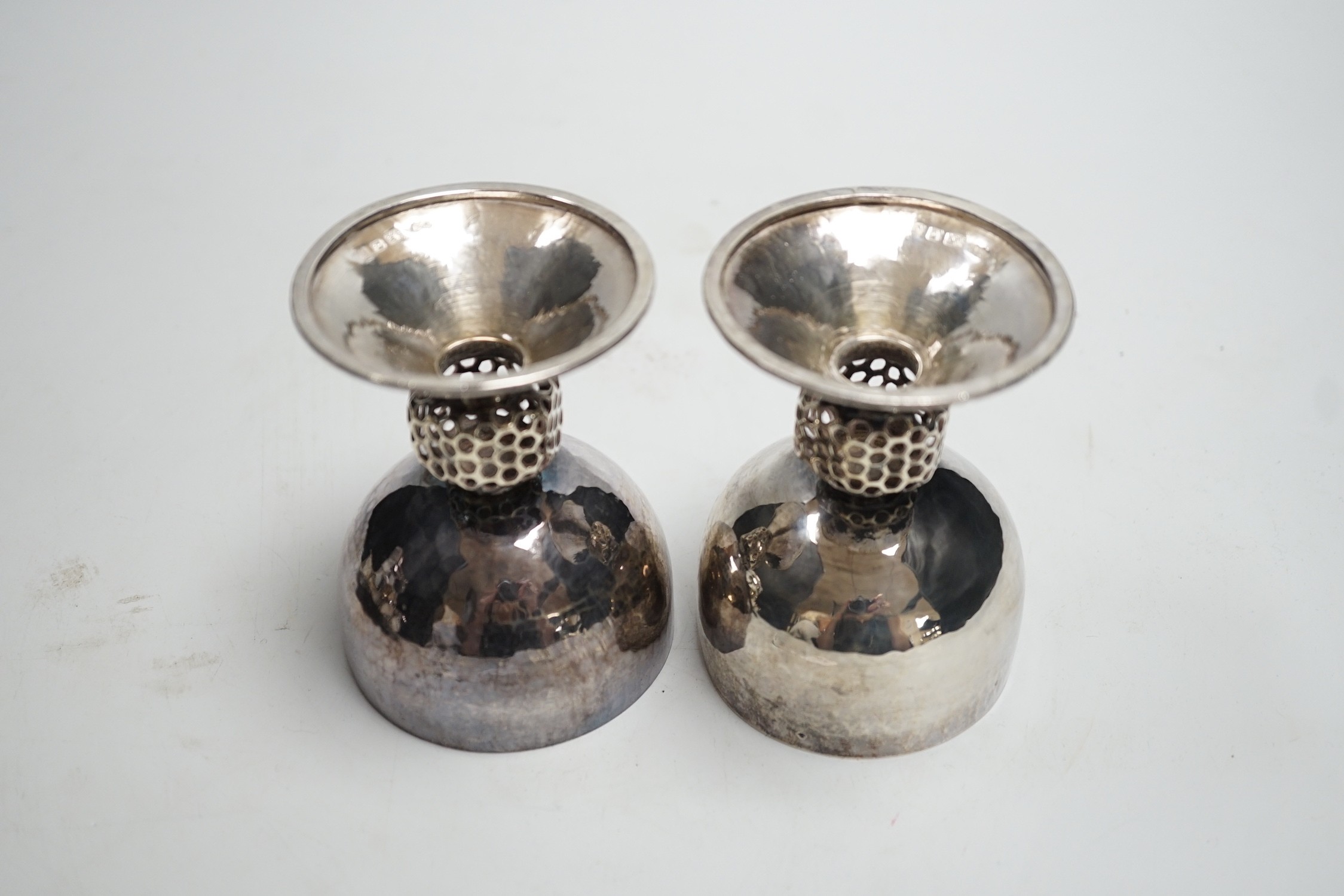 A stylish pair of Elizabeth II Arts & Crafts style planished silver pedestal cups, with reticulated stems, by Oliver Bailey, London, 1973, height 93mm, 7.5oz.